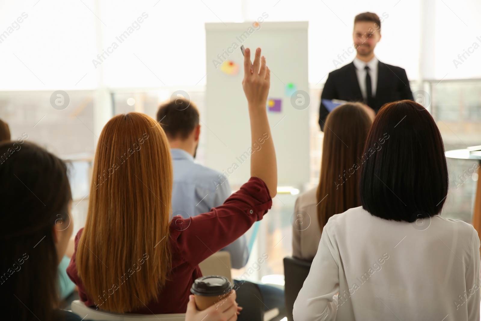 Photo of Young woman raising hand to ask question at business training indoors