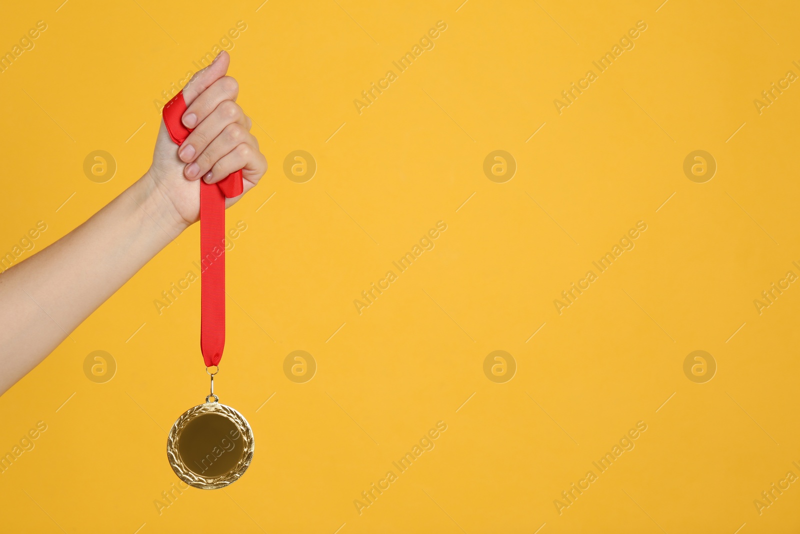 Photo of Woman holding golden medal on yellow background, closeup. Space for design