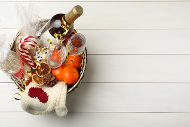 Photo of Wicker basket with Christmas gift set on white wooden table, top view. Space for text