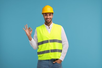 Photo of Engineer in hard hat showing ok gesture on light blue background