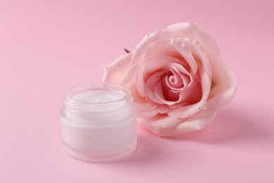 Moisturizing cream in open jar and rose flower on pink background. Body care product