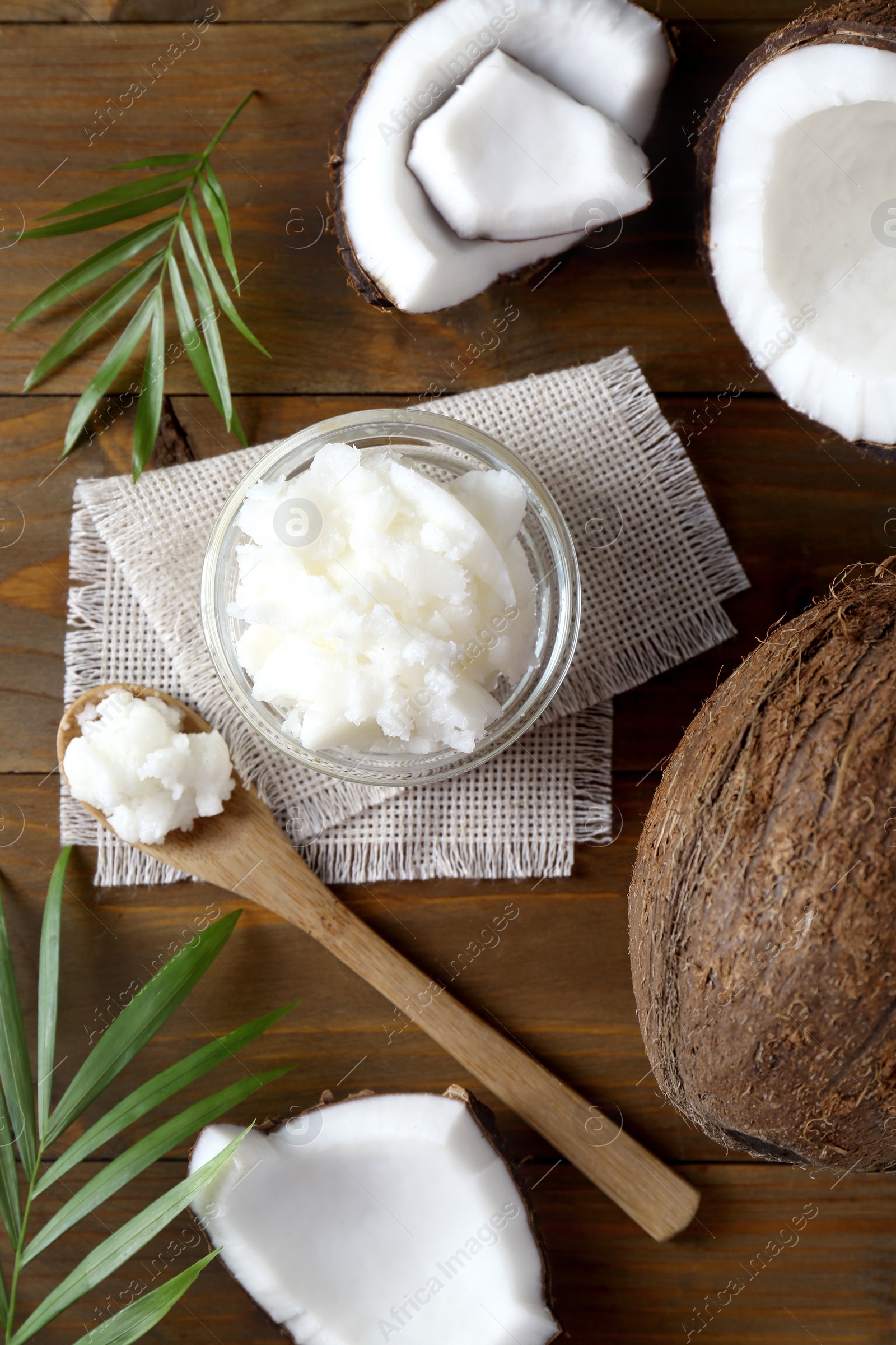 Photo of Organic coconut cooking oil, fresh fruits and leaves on wooden table, flat lay