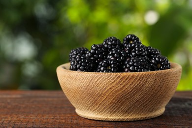 Bowl of fresh ripe blackberries on wooden table outdoors, closeup. Space for text