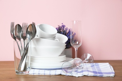 Photo of Set of clean dishes and cutlery on table against color background