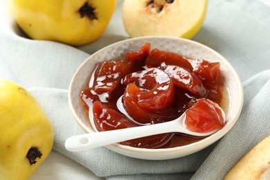 Tasty homemade quince jam in bowl, spoon and fruits on table, closeup