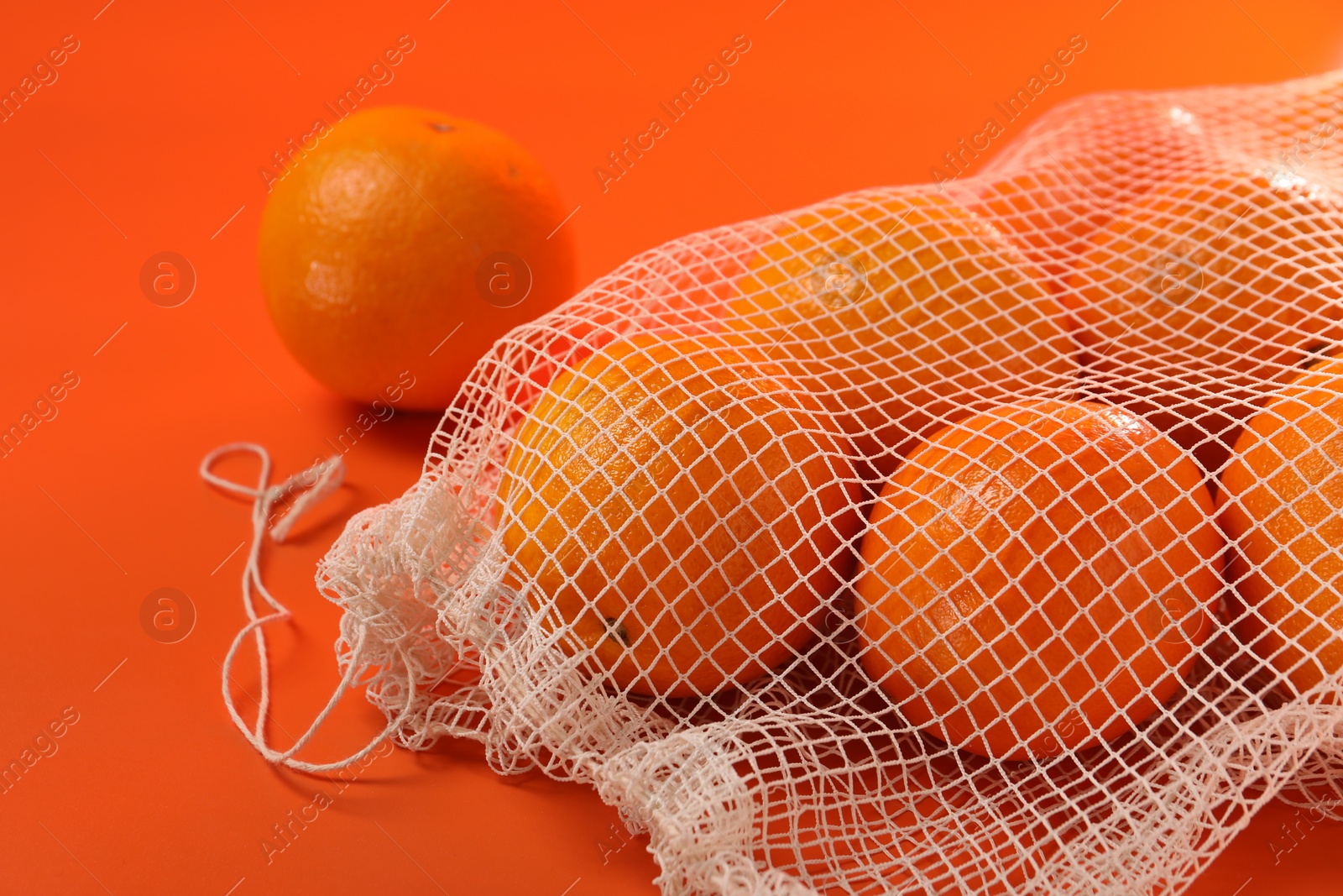 Photo of Net bag with fresh oranges on color background, closeup