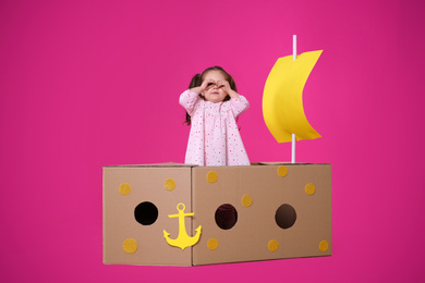 Photo of Little child playing with ship made of cardboard box on pink background