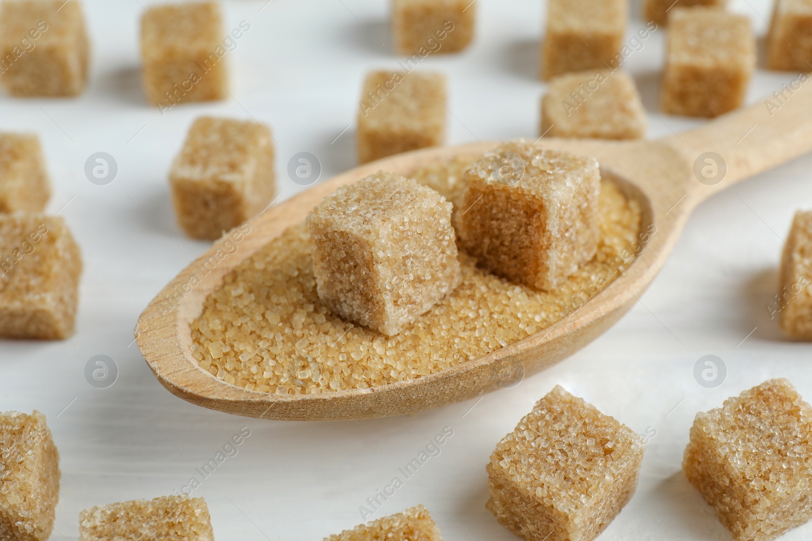 Photo of Brown sugar cubes in spoon on white wooden table, closeup