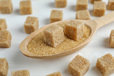 Photo of Brown sugar cubes in spoon on white wooden table, closeup