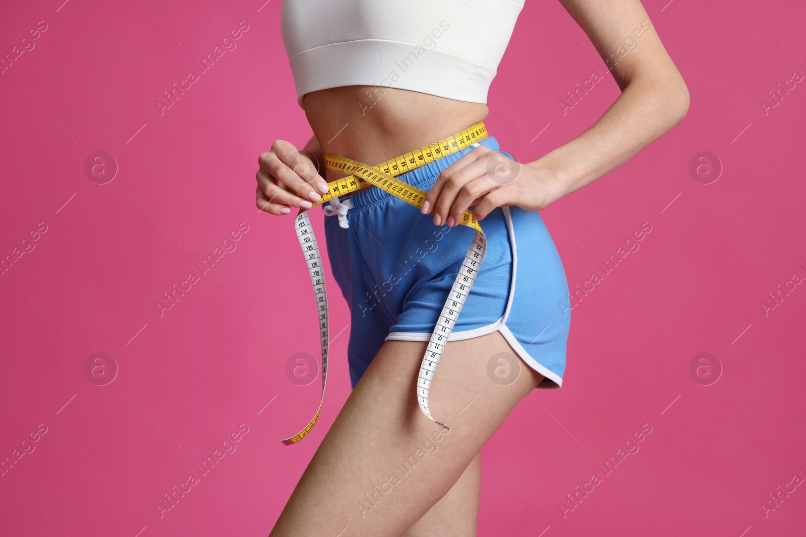 Photo of Young woman measuring waist with tape on pink background, closeup