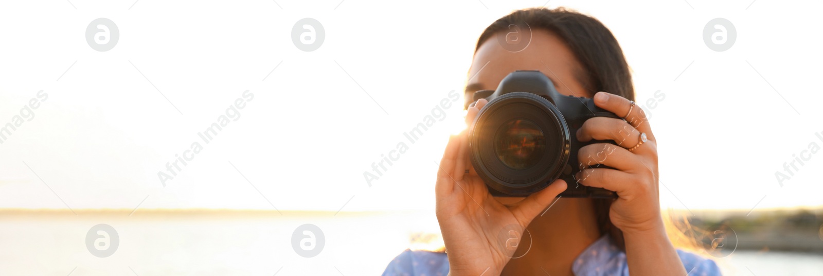 Image of Young photographer taking picture with professional camera outdoors, space for text. Banner design