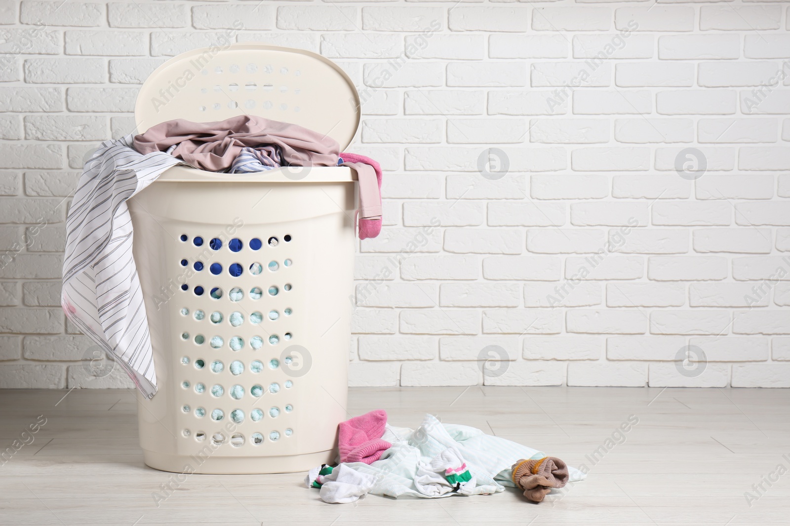 Photo of Laundry basket with clothes near white brick wall. Space for text