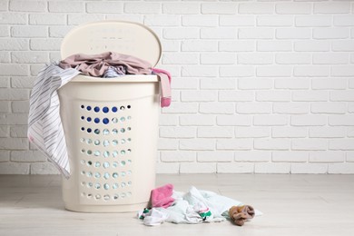 Laundry basket with clothes near white brick wall. Space for text