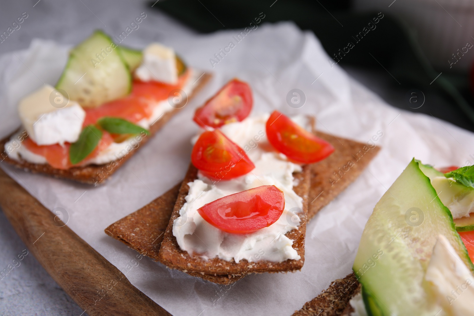 Photo of Tasty rye crispbreads with salmon, cream cheese and vegetables on parchment paper, closeup