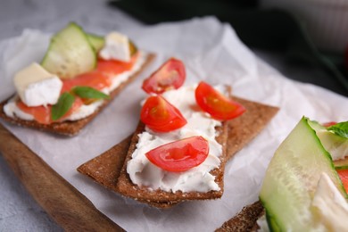 Photo of Tasty rye crispbreads with salmon, cream cheese and vegetables on parchment paper, closeup