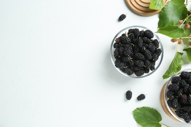 Photo of Delicious ripe black mulberries and green leaves on white table, flat lay. Space for text