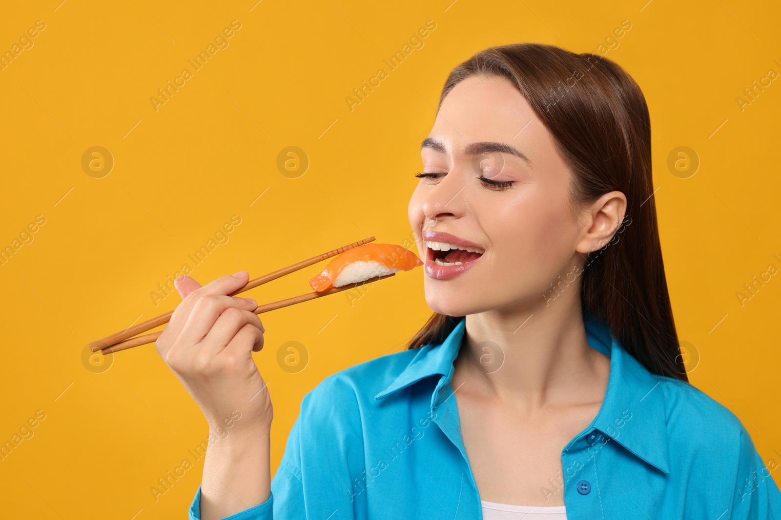 Photo of Beautiful young woman eating sushi with chopsticks on orange background