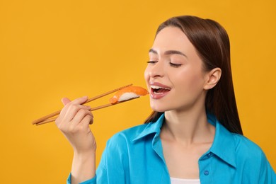 Beautiful young woman eating sushi with chopsticks on orange background