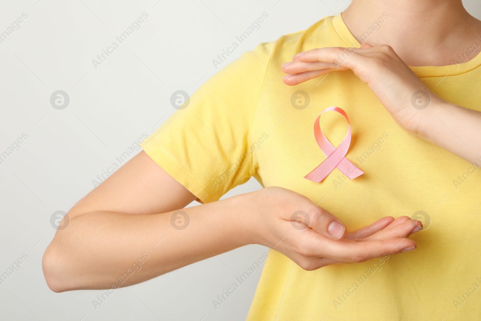 Photo of Woman with pink ribbon on t-shirt against light background. Cancer awareness