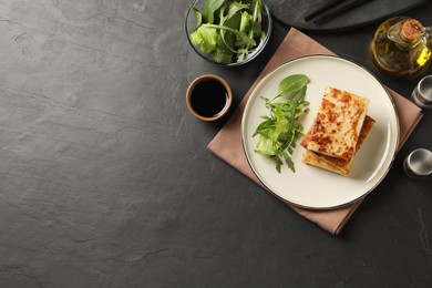 Photo of Delicious turnip cake with arugula served on black table, flat lay. Space for text