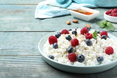Photo of Delicious cottage cheese with fresh berries and honey served on light blue wooden table, space for text. Tasty breakfast