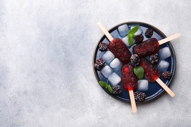 Plate of tasty blackberry ice pops and space for text on light grey table, top view. Fruit popsicle