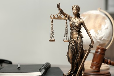 Photo of Figure of Lady Justice, gavel, globe and notebooks indoors, space for text. Symbol of fair treatment under law
