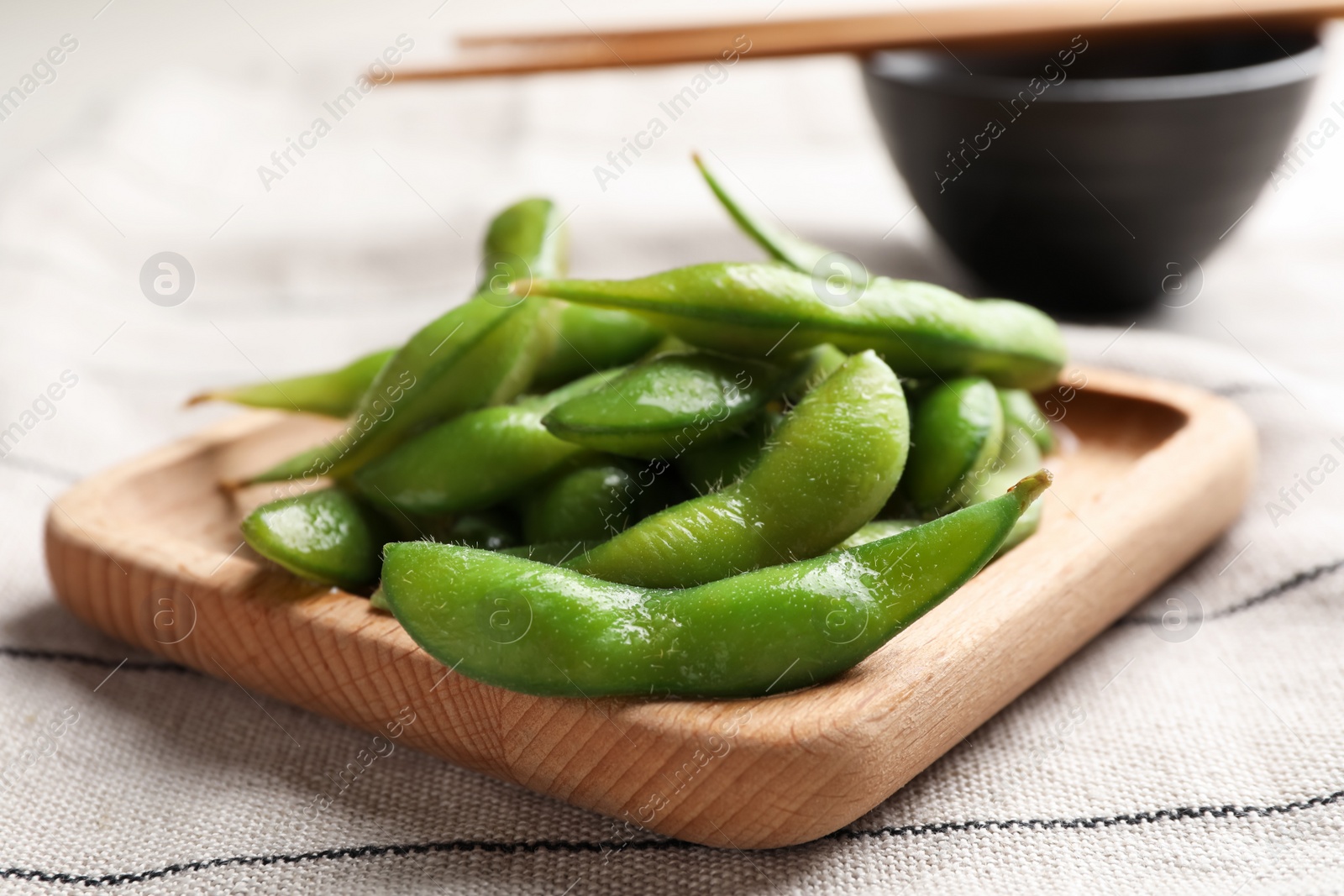 Photo of Wooden plate with green edamame beans in pods on towel, closeup