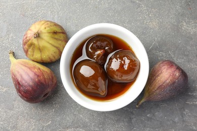 Photo of Bowl of tasty sweet jam and fresh figs on grey table