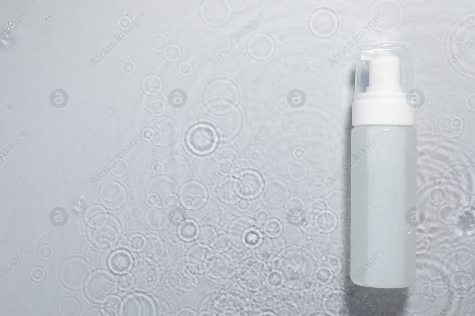 Photo of Bottle of facial cleanser in water against light grey background, top view. Space for text