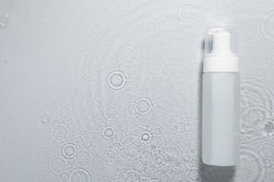 Photo of Bottle of facial cleanser in water against light grey background, top view. Space for text