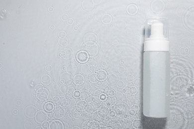 Bottle of facial cleanser in water against light grey background, top view. Space for text