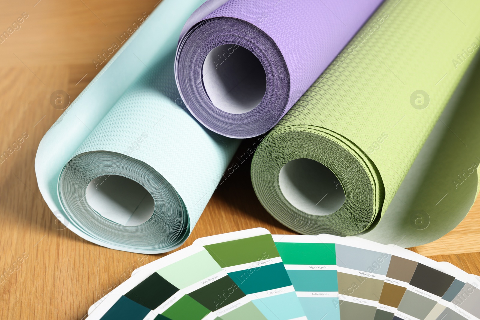 Photo of Different wallpaper rolls and color palette samples on wooden table