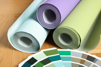 Photo of Different wallpaper rolls and color palette samples on wooden table