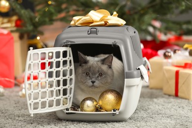 Photo of Cute cat in pet carrier near Christmas decor and gift boxes at home