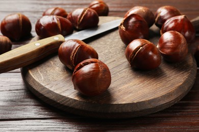 Photo of Roasted edible sweet chestnuts and knife on wooden table, closeup