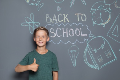 Photo of Little child near drawings and text BACK TO SCHOOL on grey background