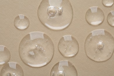 Photo of Drops of cosmetic serum on beige background, macro view