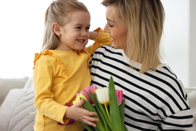 Photo of Little daughter congratulating her mom with Mother`s Day at home. Woman holding bouquet of beautiful tulips