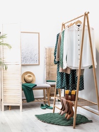 Wardrobe rack with women's clothes and shoes at color wall in room