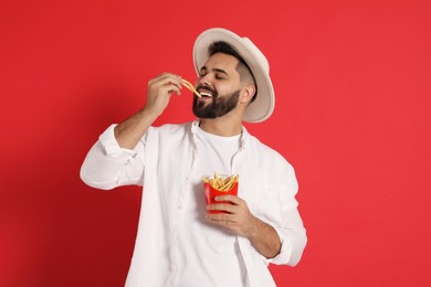 Young man eating French fries on red background