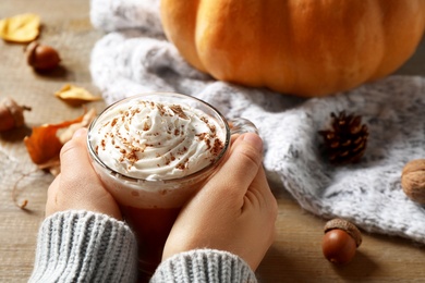 Photo of Woman with cup of pumpkin spice latte at wooden table, closeup