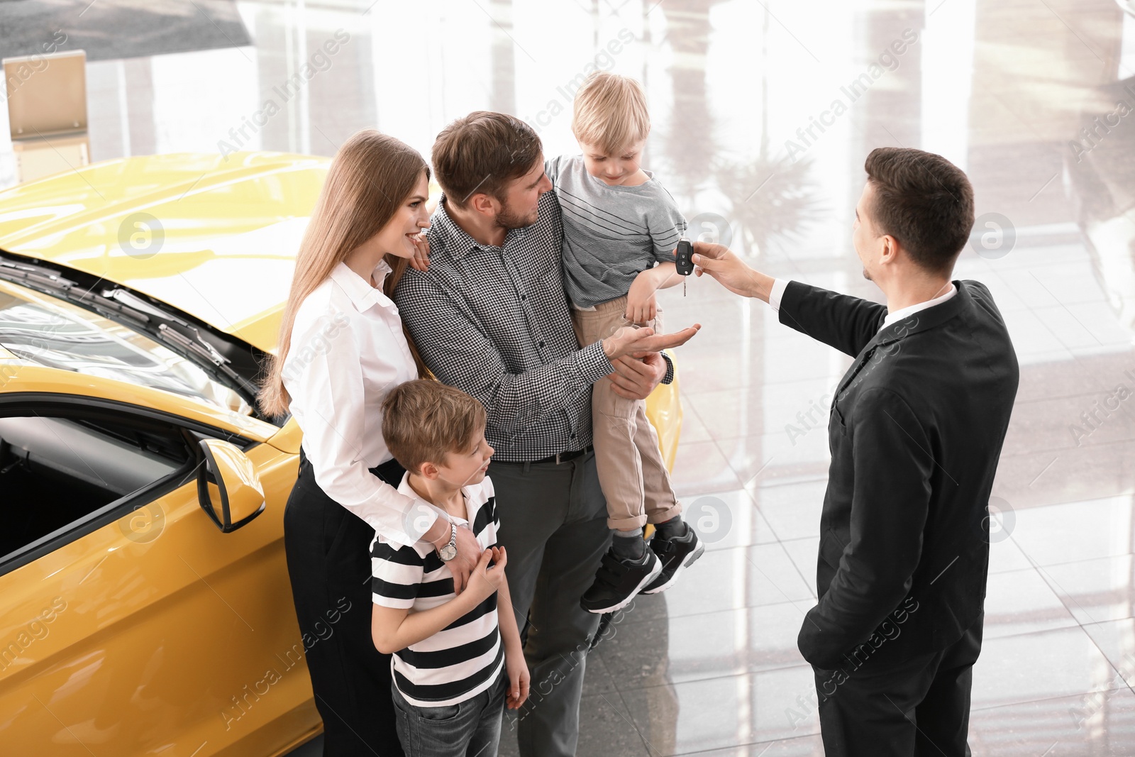 Photo of Salesman giving car key to young family in salon