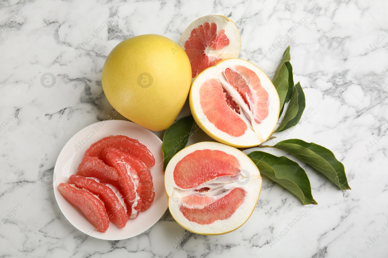 Photo of Fresh cut and whole pomelo fruits with leaves on white marble table, flat lay