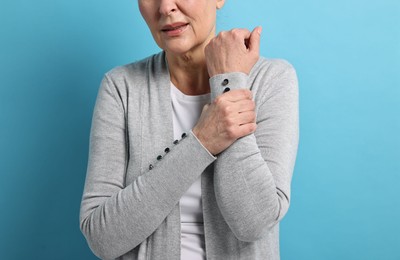 Photo of Arthritis symptoms. Woman suffering from pain in arm on light blue background, closeup