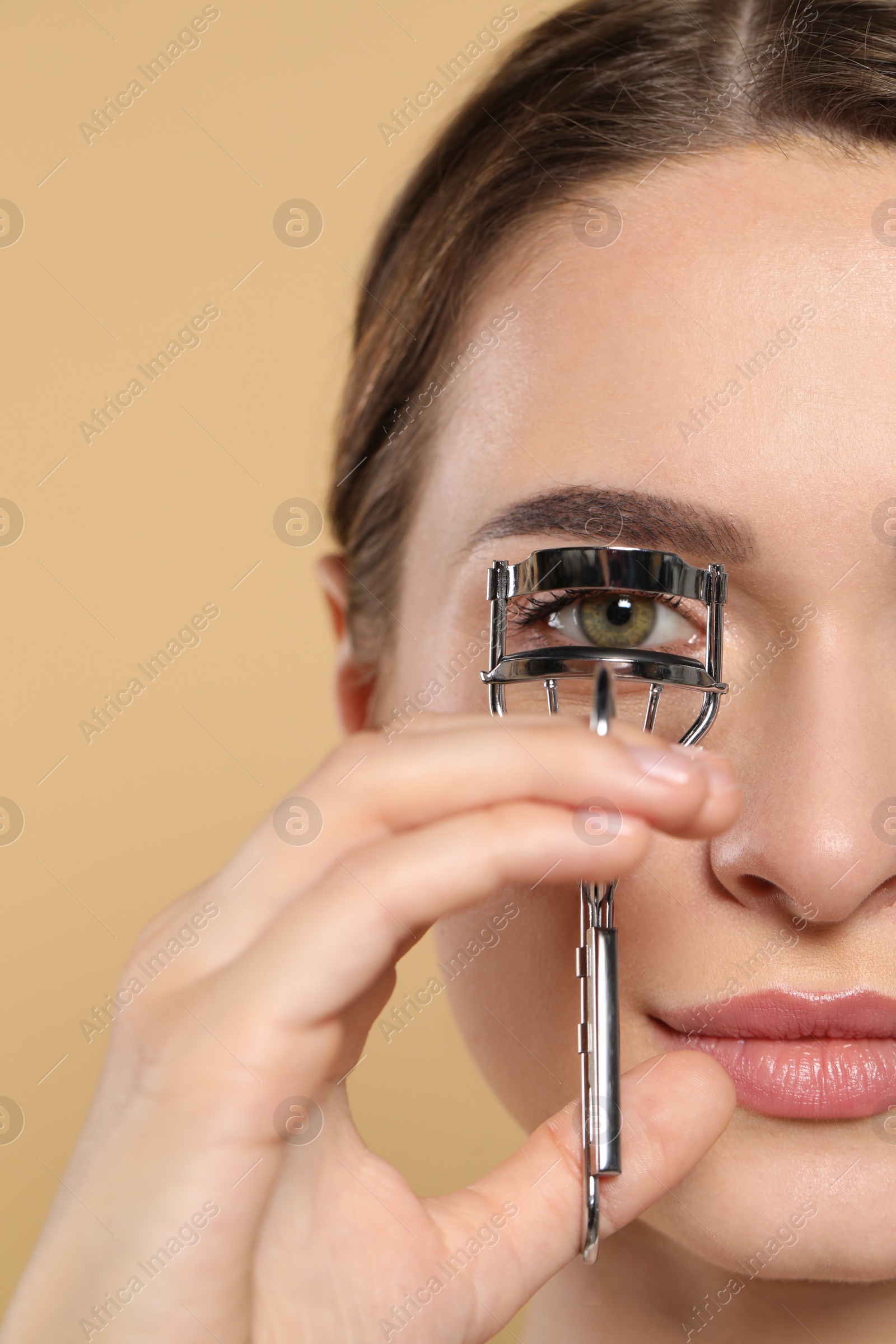 Photo of Woman using eyelash curler on beige background, closeup