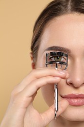 Woman using eyelash curler on beige background, closeup