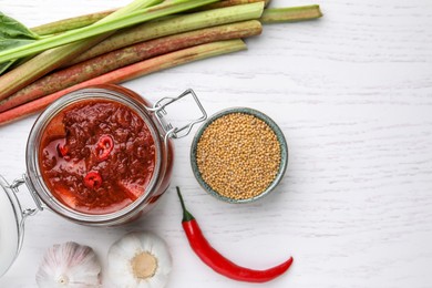 Flat lay composition with tasty rhubarb sauce and ingredients on white wooden table, space for text