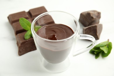 Photo of Glass cup of delicious hot chocolate, chunks and fresh mint on white table