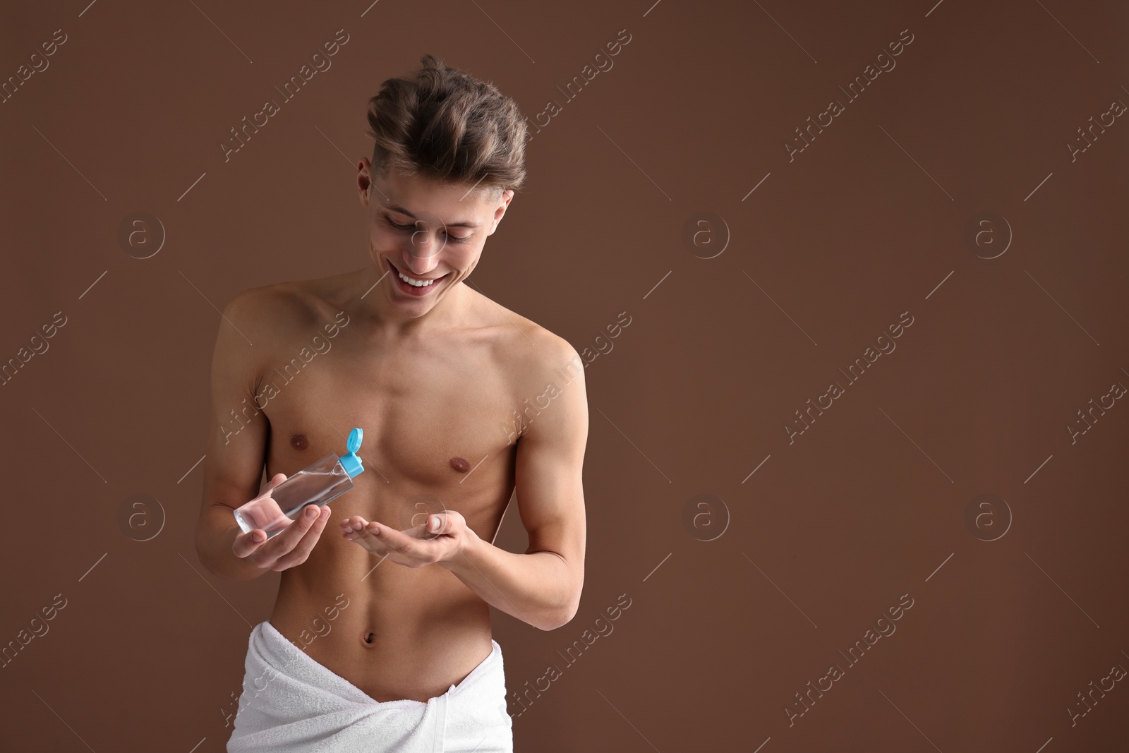 Photo of Handsome man with body lotion on brown background. Space for text